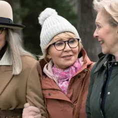 Trzy uśmiechnięte kobiety, jakby odkryły eliksir młodości, spacerują w jesiennych stylizacjach.