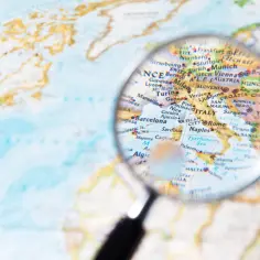 Lupa powiększa mapę Europy, ukazując kraje i regiony od Francji po Włochy i Bałkany.